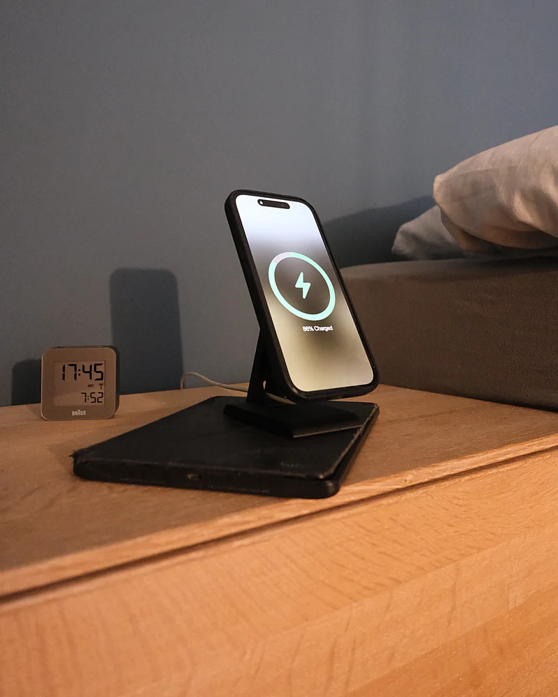 iPhone charging on the HPER, on a bedside table next to an alarm clock
